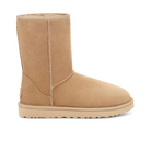 The UGG Womens Classic Short II Boot in Mustard Seed is a tan suede, mid-calf boot with a rounded toe, flat sole, visible stitching, and plush sheepskin lining for comfort. Displayed side profile on a white background.