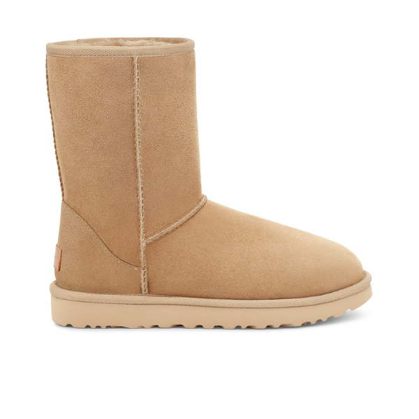 The UGG Womens Classic Short II Boot in Mustard Seed is a tan suede, mid-calf boot with a rounded toe, flat sole, visible stitching, and plush sheepskin lining for comfort. Displayed side profile on a white background.