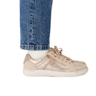 A person in blue jeans, white socks, and CLARKS Women's Nalle Zen Metallic sneakers with white soles and side zippers stands against a plain white background.