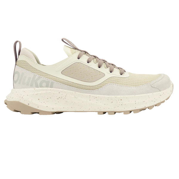 The OLUKAI Women's Makiki Lava White Sand is a beige and light tan athletic shoe with a mesh upper, textured sole, speckled midsole, lace-up closure, and heel pull tab—ideal for all-terrain trail running.