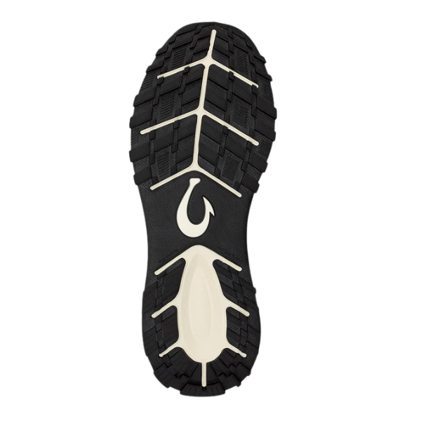 The image shows the black and white treaded sole of an OLUKAI Men's Makiki Grey shoe, viewed from underneath, featuring a unique wavy logo near the arch and providing trail-ready traction for all-terrain use.