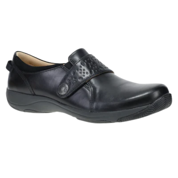 The Dansko Women's Sallie Black is a leather slip-on featuring a textured, perforated strap and low rubber sole, offering orthotic-friendly comfort for casual wear.
