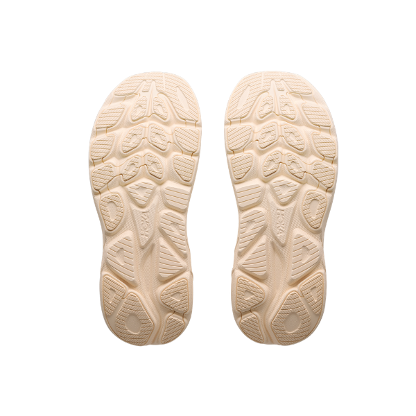 HOKA Women's Clifton 11 Wide Alab/Oat trainers feature beige cushioned soles with geometric tread, shown on white.