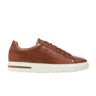 The Birkenstock Men’s Bend Low Cognac sneaker by BIRKENSTOCK features brown natural leather, matching laces, a white rubber sole with cork detail, and signature support, shown in side view on a white background.