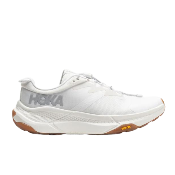 The HOKA Women’s Transport White is a sustainable, low-cut running shoe with a thick sole, gray HOKA logo, brown rubber outsole accents, and modern athletic styling designed for comfort and foot pain relief.