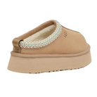 The UGG Womens Tazz Slippers Sand by UGG feature a tan slip-on design, thick platform outsole, soft UGGplush lining, and decorative stitching around the opening, shown from the back.