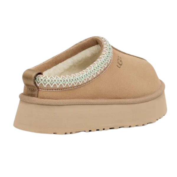 The UGG Womens Tazz Slippers Sand by UGG feature a tan slip-on design, thick platform outsole, soft UGGplush lining, and decorative stitching around the opening, shown from the back.