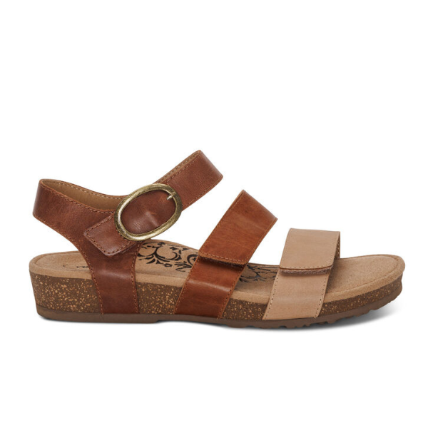 The Aetrex Women's Lilly Adjustable Quarter Strap Sandal in Walnut by AETREX WORLDWide INC features brown and tan leather straps, a low cork sole, arch support, a brass ankle buckle, and a floral footbed pattern near the heel.