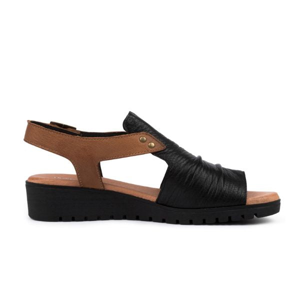 The Django & Juliette Womens Madis Black Leather sandal by DJANGO & JULIETT features a black ruched open toe, brown ankle strap with gold rivets, low black wedge heel, and a soft leather footbed. Side profile shown on a white background.