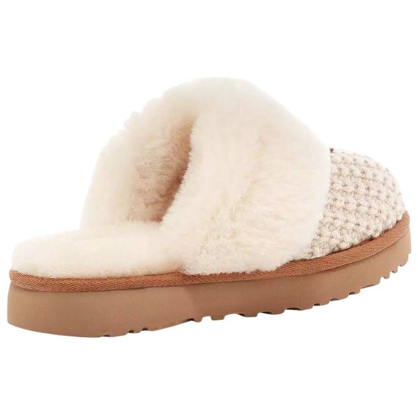The UGG Women's Cozy Cream slipper features a sheepskin lining and tan rubber sole, shown from the back and side.