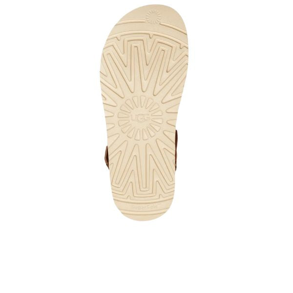 The UGG Womens Goldenstar Clog Chestnut features a beige rubber sole with an embossed geometric tread and the UGG logo at the center, displayed on a white background.