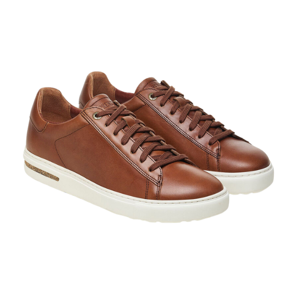The Birkenstock Mens Bend Low Cognac sneakers feature brown natural leather, white rubber soles, brown laces, and a contoured footbed for signature BIRKENSTOCK support, shown on a white background.