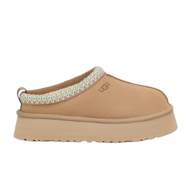 The UGG Womens Tazz Slippers Sand feature a tan color, platform outsole, decorative white stitching around the opening, soft UGGplush lining, and the UGG logo on the side.
