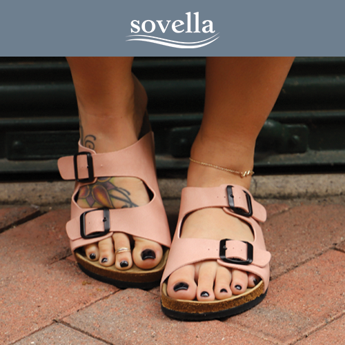 Person wearing pink sandals with black nail polish and a tattoo on foot, standing on brick pavement; sovella logo above.