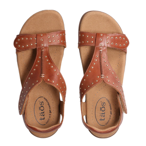 A pair of TAOS Womens Show Stopper Cognac sandals in brown leather with metallic studs, open toes, and adjustable straps, shown from above. Features Soft Support insoles with Cool Recovery Foam and TAOS branding near the heel.