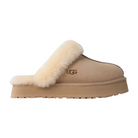 The UGG Womens Disquette Sand slipper features signature sheepskin and suede with a thick, fluffy trim and retro-style platform sole, shown in side view on a white background.