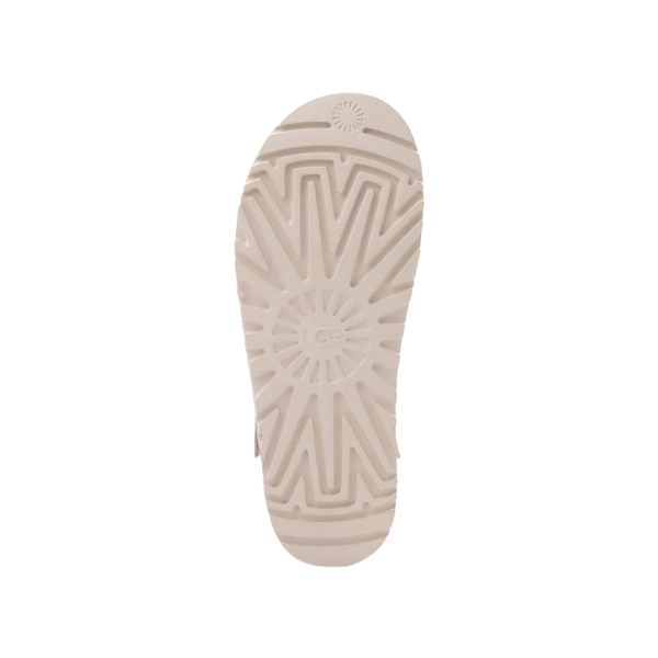 The image shows the beige sole of the UGG Womens Goldenstar Bay Fog sandal, featuring geometric and sunburst tread patterns with a circular UGG logo in the center, set against a white background.