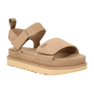 The UGG Womens Goldenstar Sand is a tan suede platform sandal with adjustable hook-and-loop straps, a cushioned sole for comfort, a ridged rubber outsole, and UGG embossed on the upper strap.