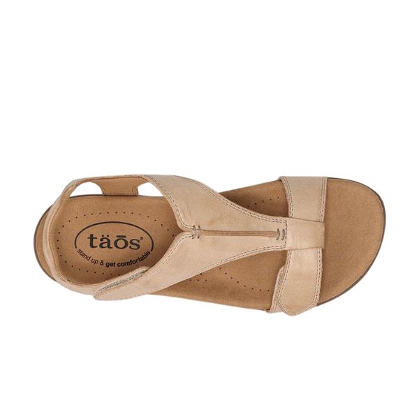 A top view of the Taos Womens The Show Stone sandal in tan leather features a cushioned insole, arch support, open toe, and TAOS logo on the heel.