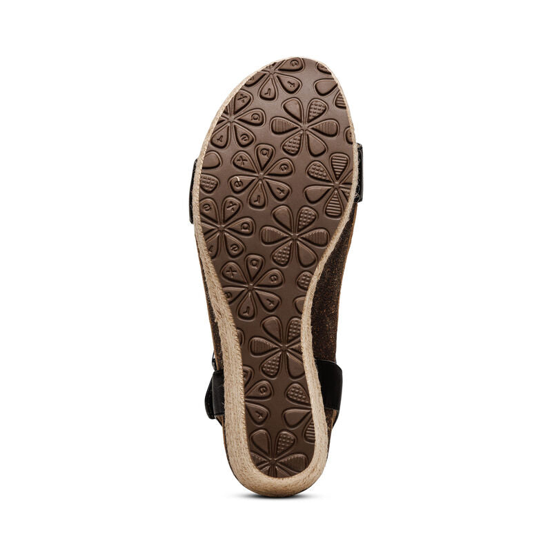 The image displays the bottom view of the Aetrex Womens Sydney Black Leather sandal, featuring a brown sole with a raised floral grip pattern and textured, light edges that complement its memory foam footbed by Aetrex.