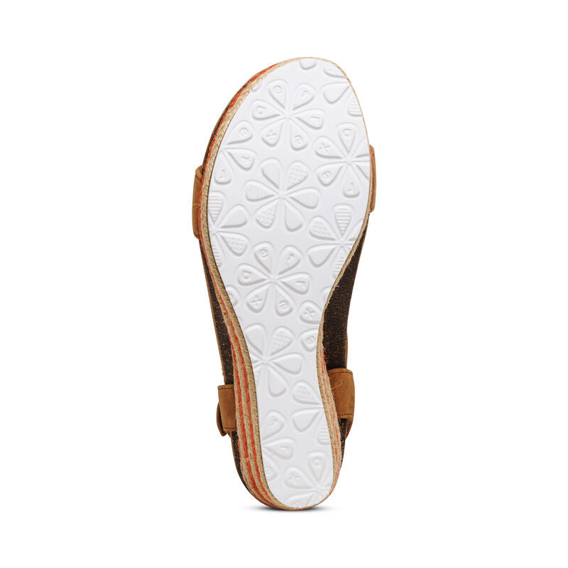 The image shows the bottom view of the Aetrex Womens Sydney Cognac sandal. It features a white rubber sole with floral patterns, a brown upper with cork-like edging, and built-in arch support for enhanced comfort.