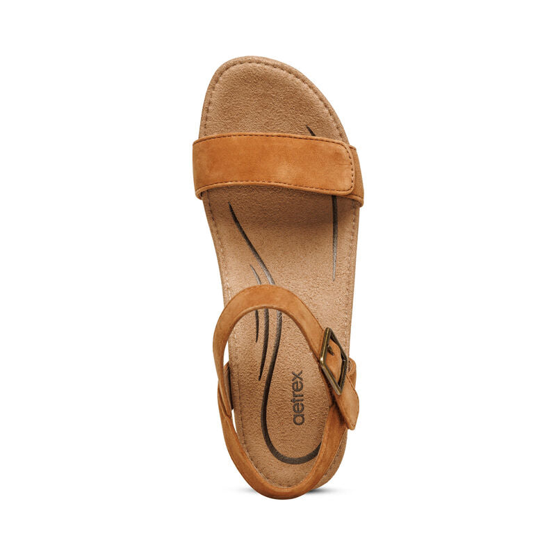 The Aetrex Womens Sydney Cognac sandal features an adjustable espadrille strap with buckle, a cushioned memory foam footbed with arch support, and the Aetrex logo near the heel, all shown against a white background.