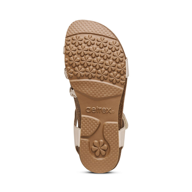The image shows the bottom view of the Aetrex Womens Jillian Ivory sandal, featuring textured floral patterns and circular grips on the sole for traction, with the Aetrex brand name embossed in the center and a supportive orthotic footbed.