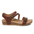 The Aetrex Womens Jillian Walnut sandal features brown leather, a low cork wedge heel, braided and smooth adjustable straps, decorative metal buttons, and a floral pattern on the cushioned footbed.