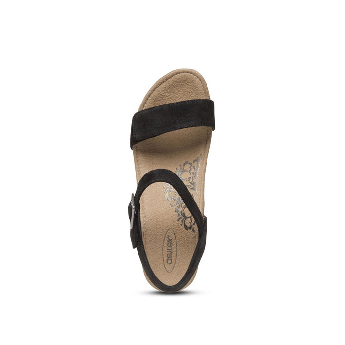 Top view of a single Aetrex Womens Sydney Black sandal with black straps over the toe and ankle, a tan cushioned insole with floral design, arch support, and Aetrex branding printed on it.